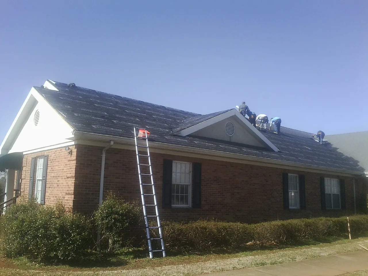 Crew tearing shingles off a brick ranch roof with a ladder set — Emergency Roof Repair work by our crew in Norwood